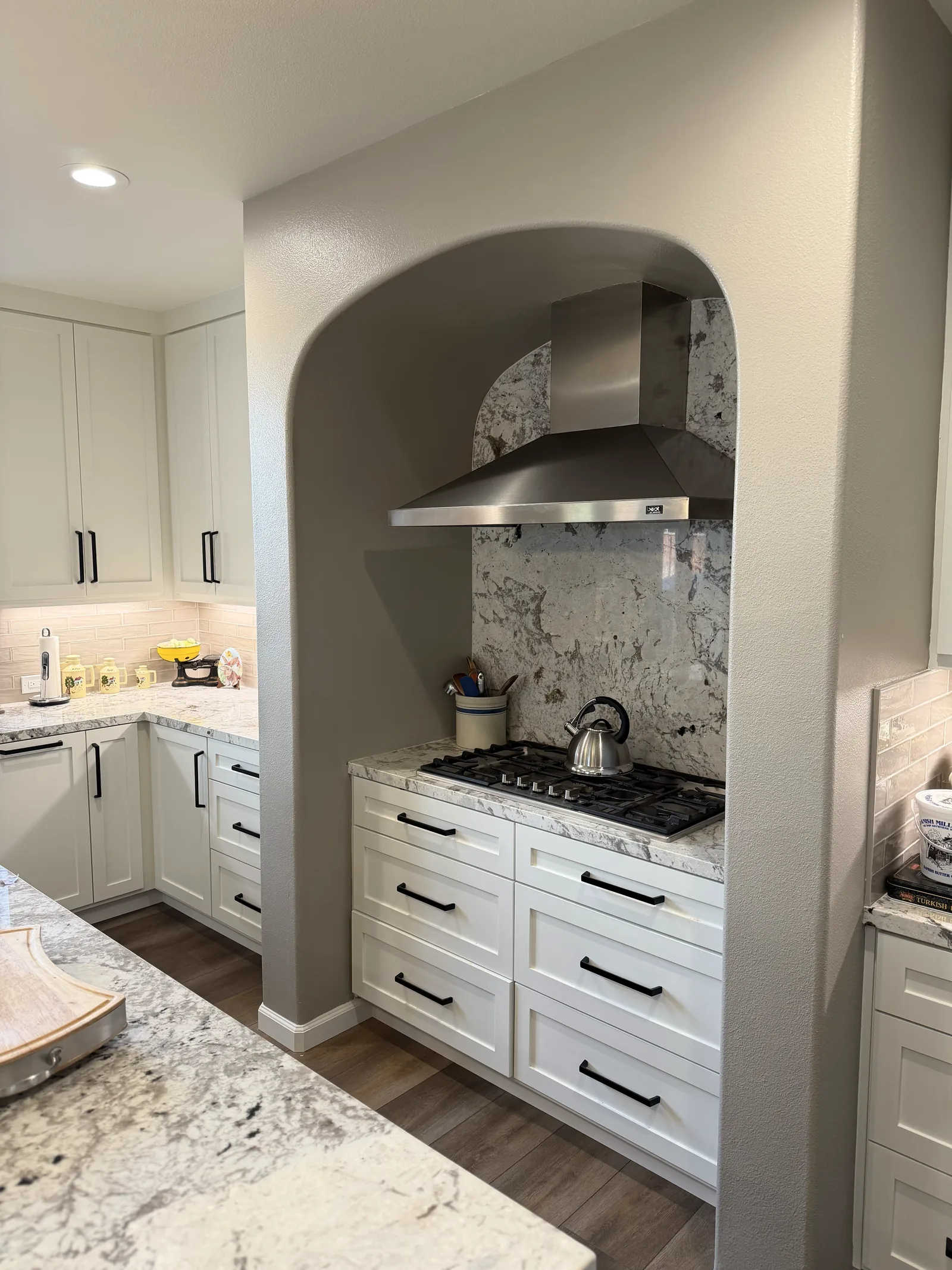 White shaker kitchen with an arched hood niche and granite backsplash in Gilroy