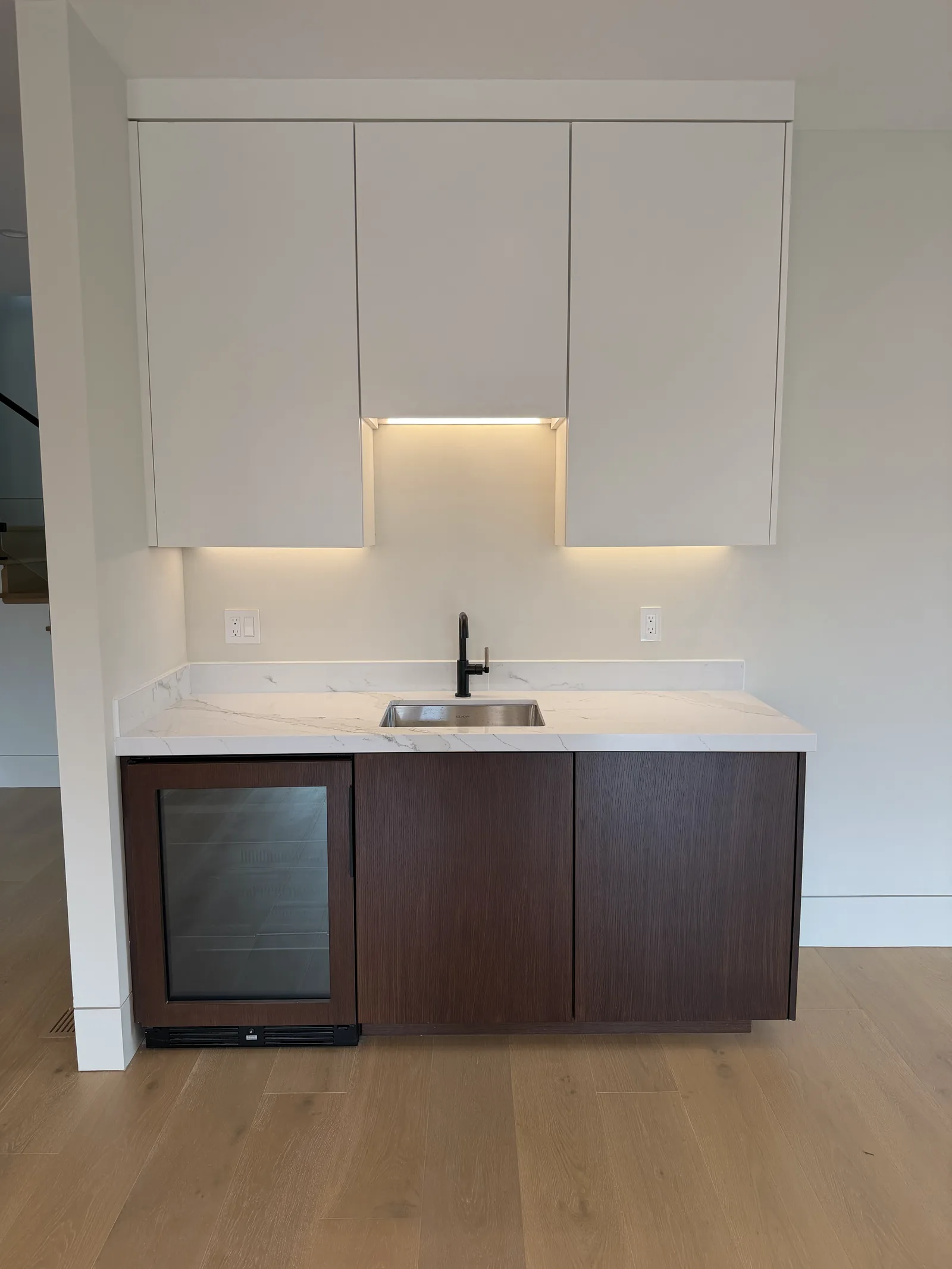Dark walnut home bar with a built-in wine fridge and white uppers in Los Altos