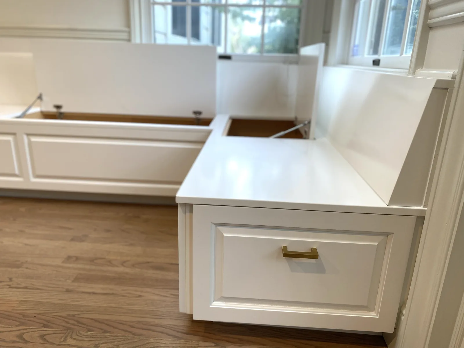 White built-in bench seating with brass cup pulls along a window in Los Gatos