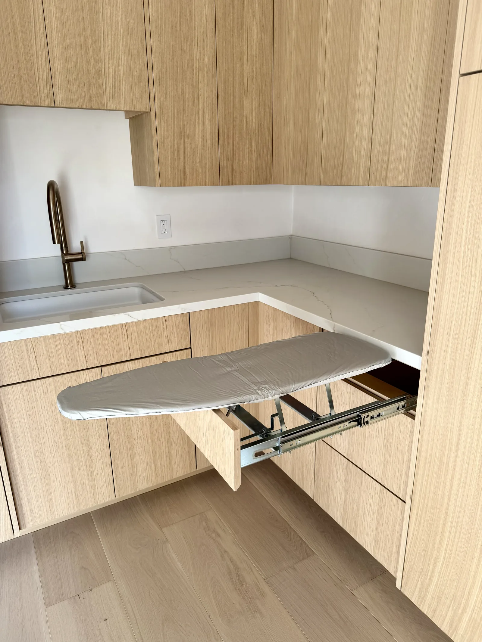 Concealed pull-out ironing board built into a white oak cabinet run in Monterey