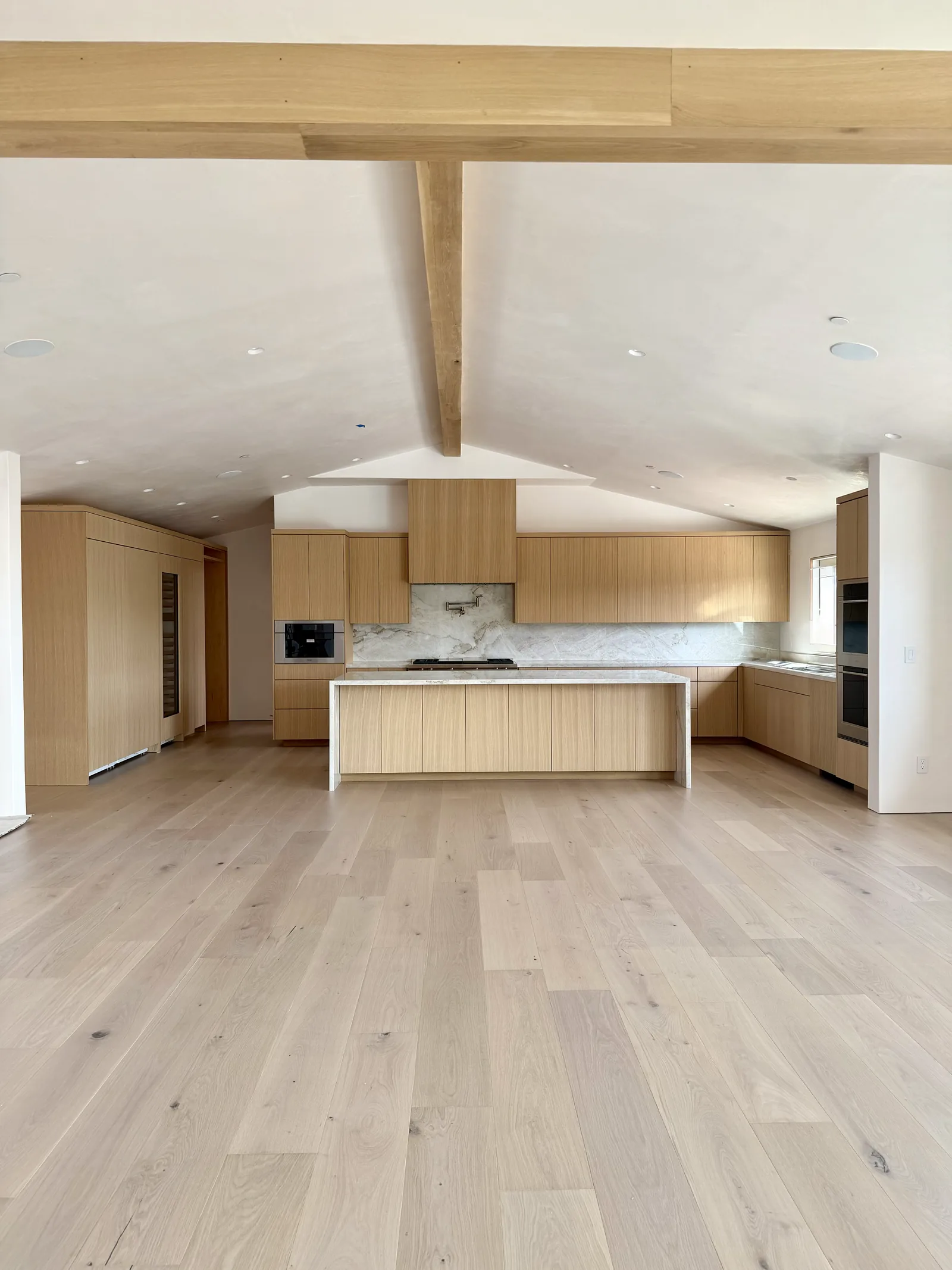 Open plan white oak kitchen with exposed beams and a marble island in Monterey