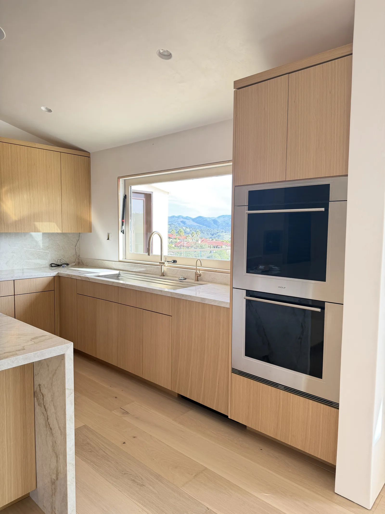 White oak kitchen run with built-in wall ovens and a quartz counter in Monterey