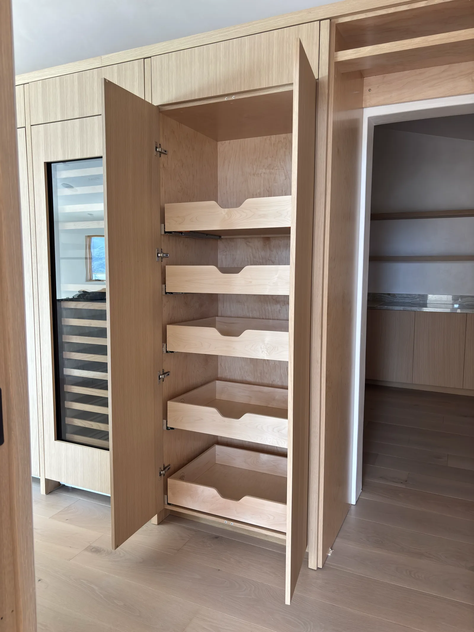 White oak pantry with pull-out shelves and a built-in wine fridge in Monterey