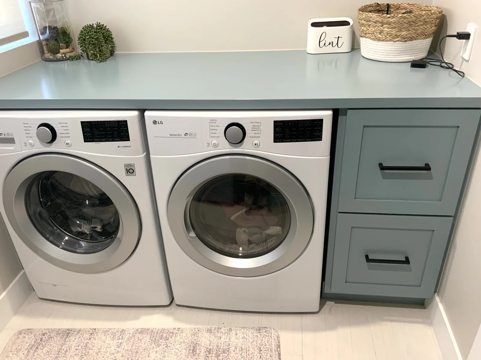 Sage green laundry cabinets with a folding counter over the machines in San Jose