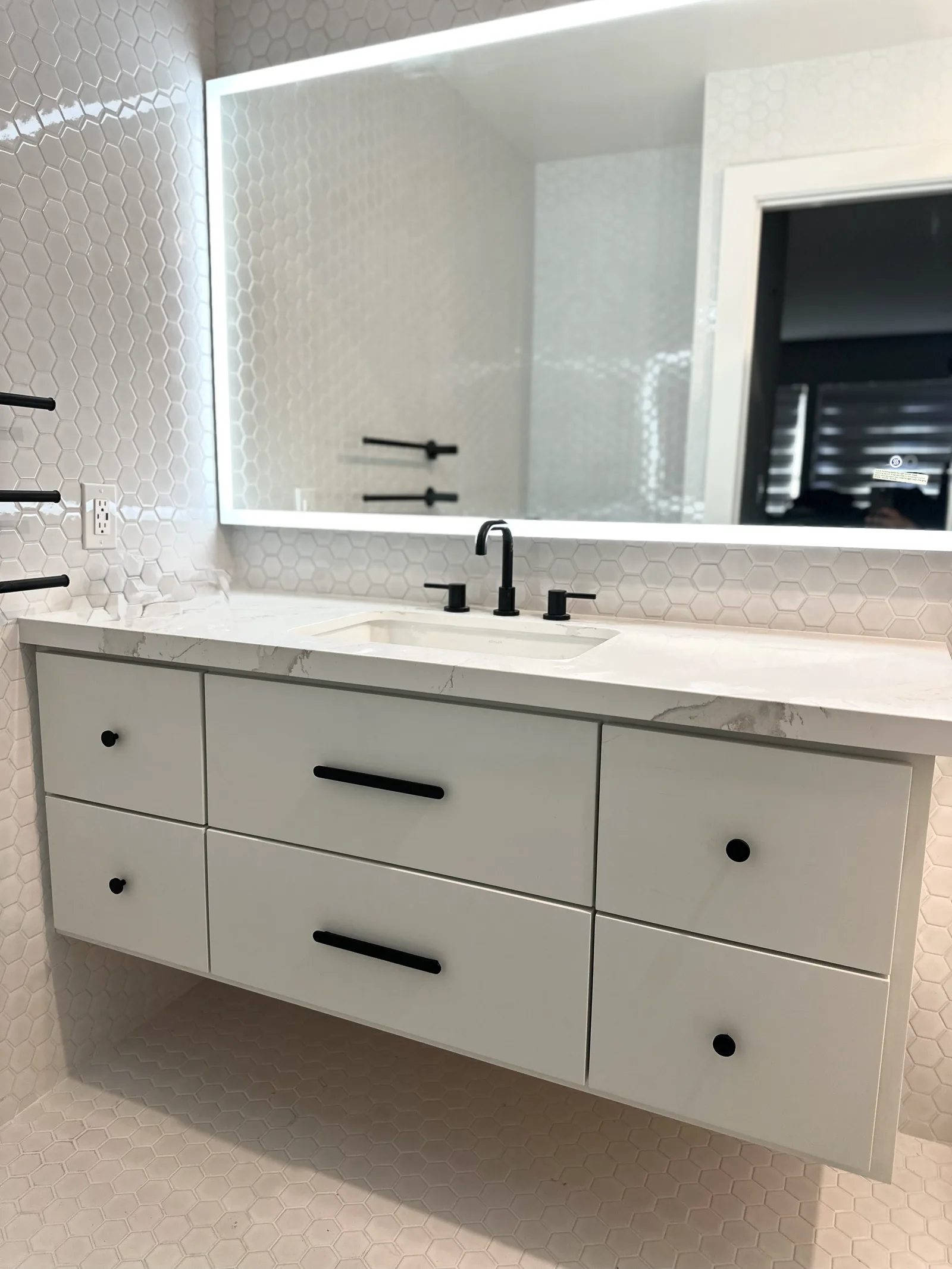 White floating vanity with matte black hardware and a lit mirror in San Jose